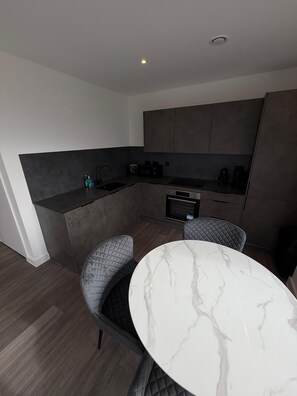 A modern kitchen with dark cabinetry, a built-in microwave, and a small dining area with a marble table and two cushioned chairs. - Stunning 2 Bedroom Apartment-2 Bath with Balcony (Salford)