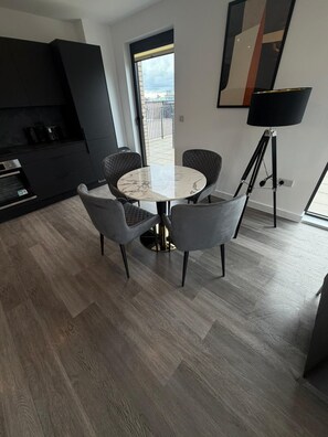 A modern kitchen with dark cabinetry, a built-in oven, and a dining area with a round table and four chairs. - Stunning 2 Bedroom Apartment-2 Bath with Balcony (Salford)