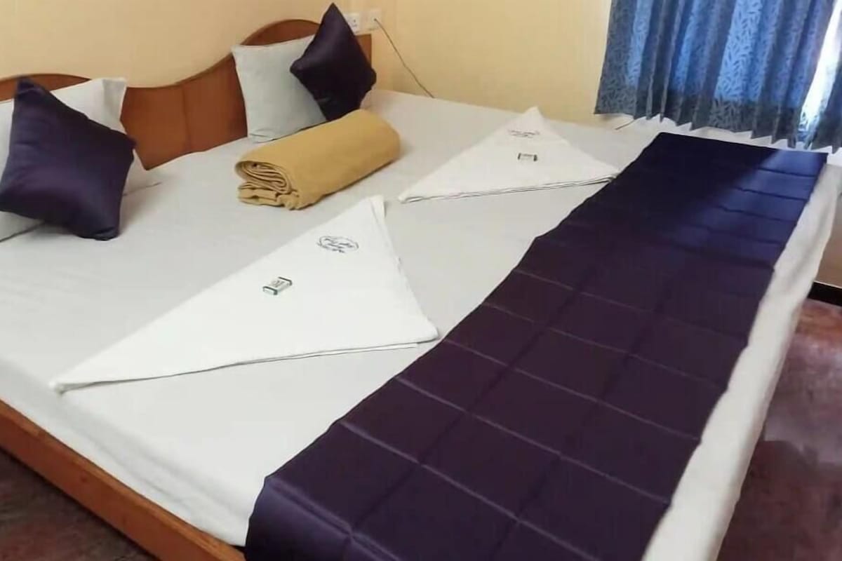 A bed with a white mattress, two pillows, a folded towel, and a dark blue bedspread.
