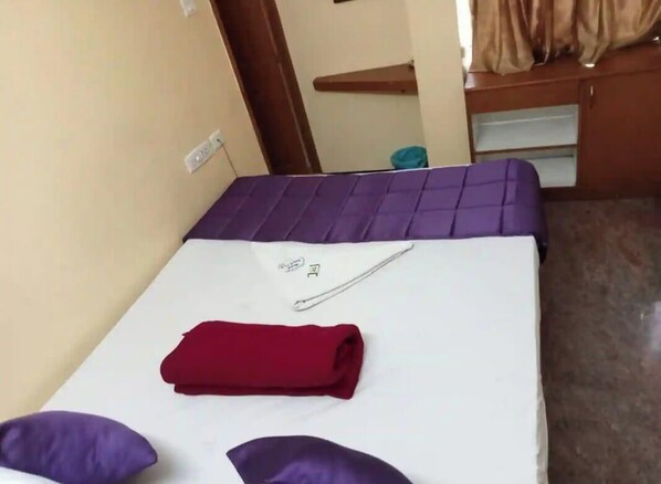 A single bed with a purple headboard and a red blanket, a white pillow, and a small white object on the bed. - Hotel Royal Park (Coimbatore)