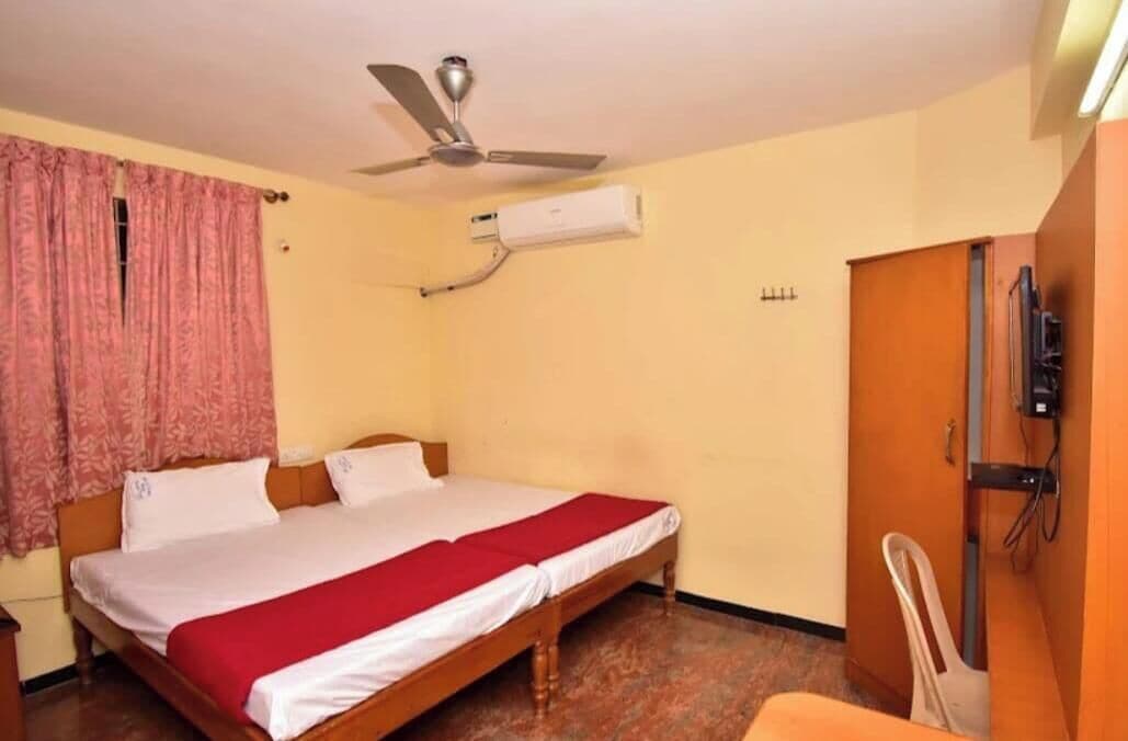 A single bed with a wooden frame, a ceiling fan, an air conditioning unit, and a door with a handle.