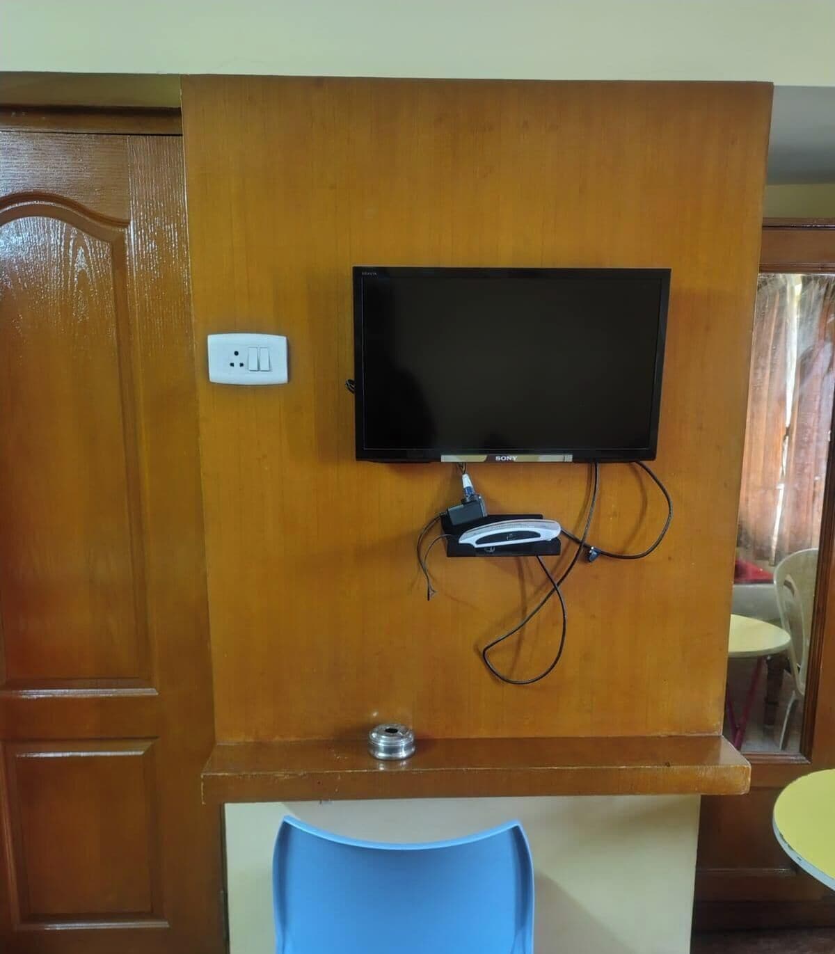A television mounted on a wooden wall with a power outlet and a cable management system below it.