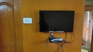 A television mounted on a wooden wall with a power outlet and a cable management system below it. - Hotel Royal Park (Coimbatore)