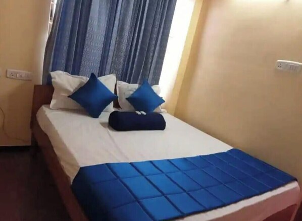A bed with a blue bedspread and pillows, a wooden headboard, and a window with curtains.