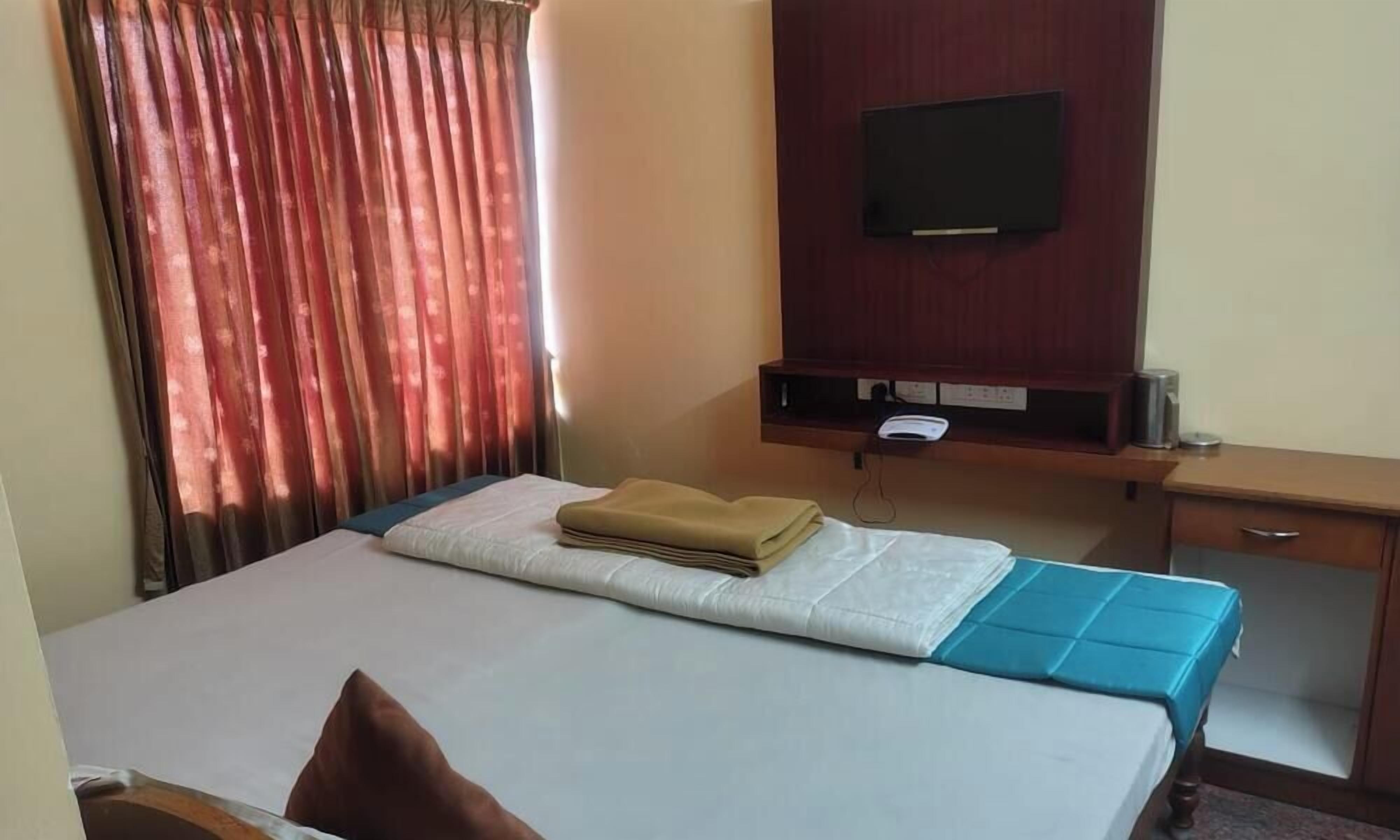 A hotel room with a bed, a desk, a television mounted on the wall, and a window with curtains.