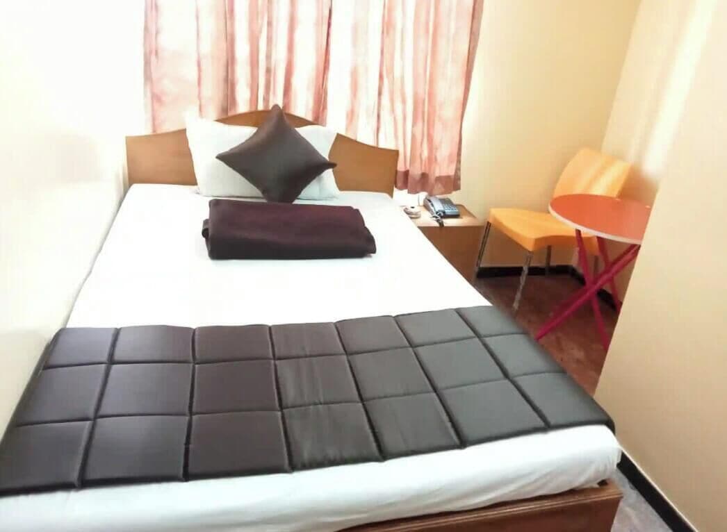 A hotel room with a bed, a bedside table with a phone and remote, a chair, and curtains.