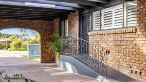 A brick building with a covered entrance, a metal staircase, and a white fence in the background. - Sandy Toes Haven a Lux Pet-Friendly Retreat (Nelson Bay)