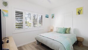 Une chambre à coucher avec un lit, un bureau en bois et une fenêtre avec des stores.