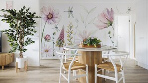 Un coin repas avec une table ronde, des chaises blanches et une fresque murale représentant des motifs floraux et des insectes.