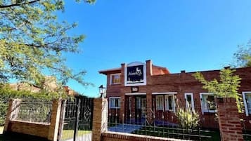 A brick building with a gated entrance, a sign reading 'AIMATA,' and a clear blue sky.