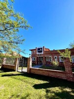 A brick building with a gated entrance, a sign reading 'AIMATA,' and a clear blue sky.