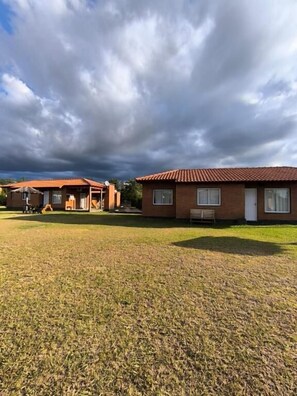 A residential property with a grassy lawn, a brick house with a tiled roof, and a clear sky. - Hotel Aimara  (Mina Clavero)
