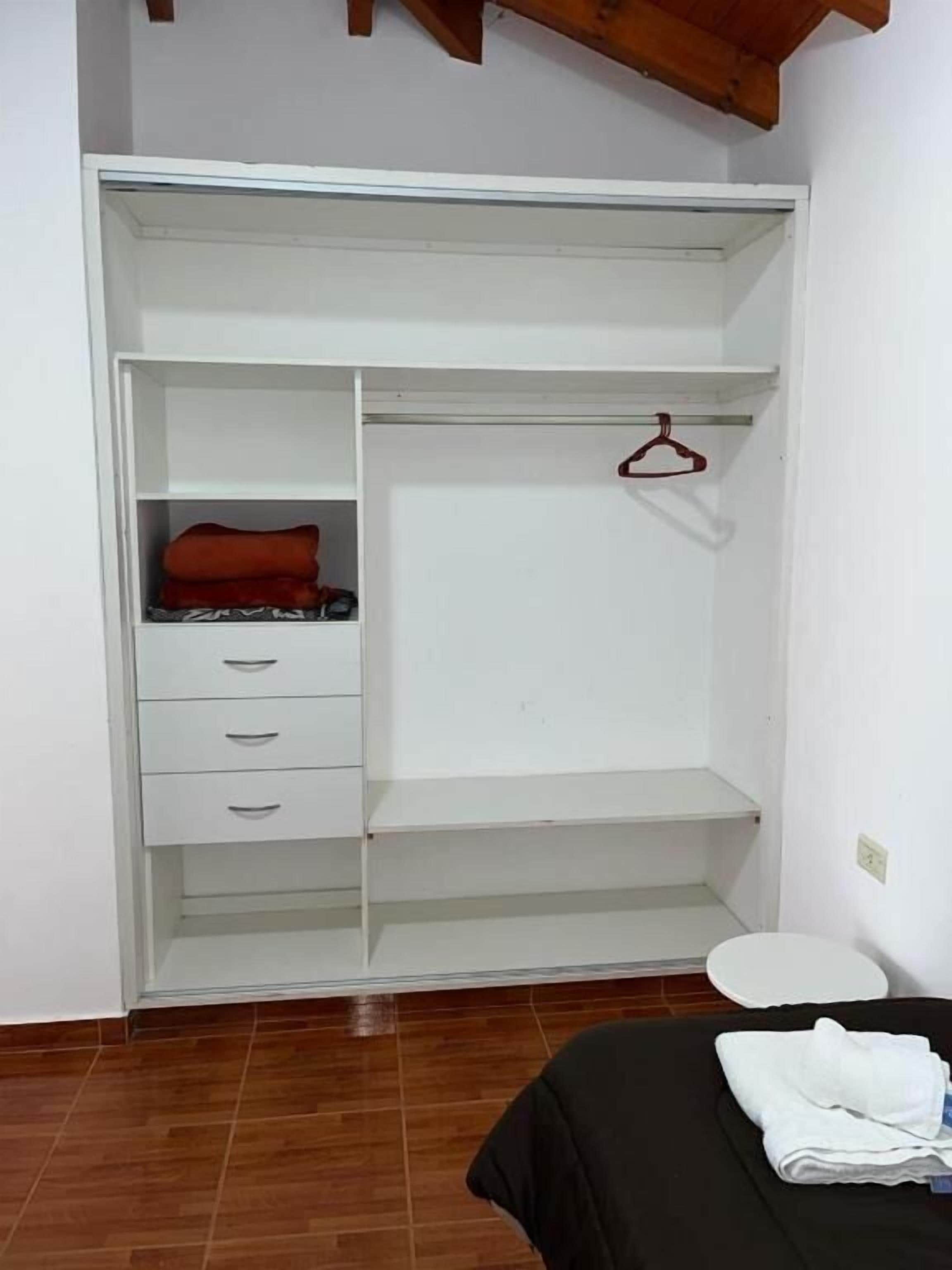 Une pièce avec une armoire blanche, un lit recouvert d’une couverture noire et des toilettes blanches.