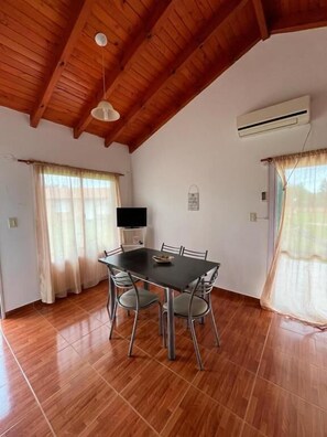 A dining area with a wooden ceiling, a table with chairs, and an air conditioning unit on the wall.
