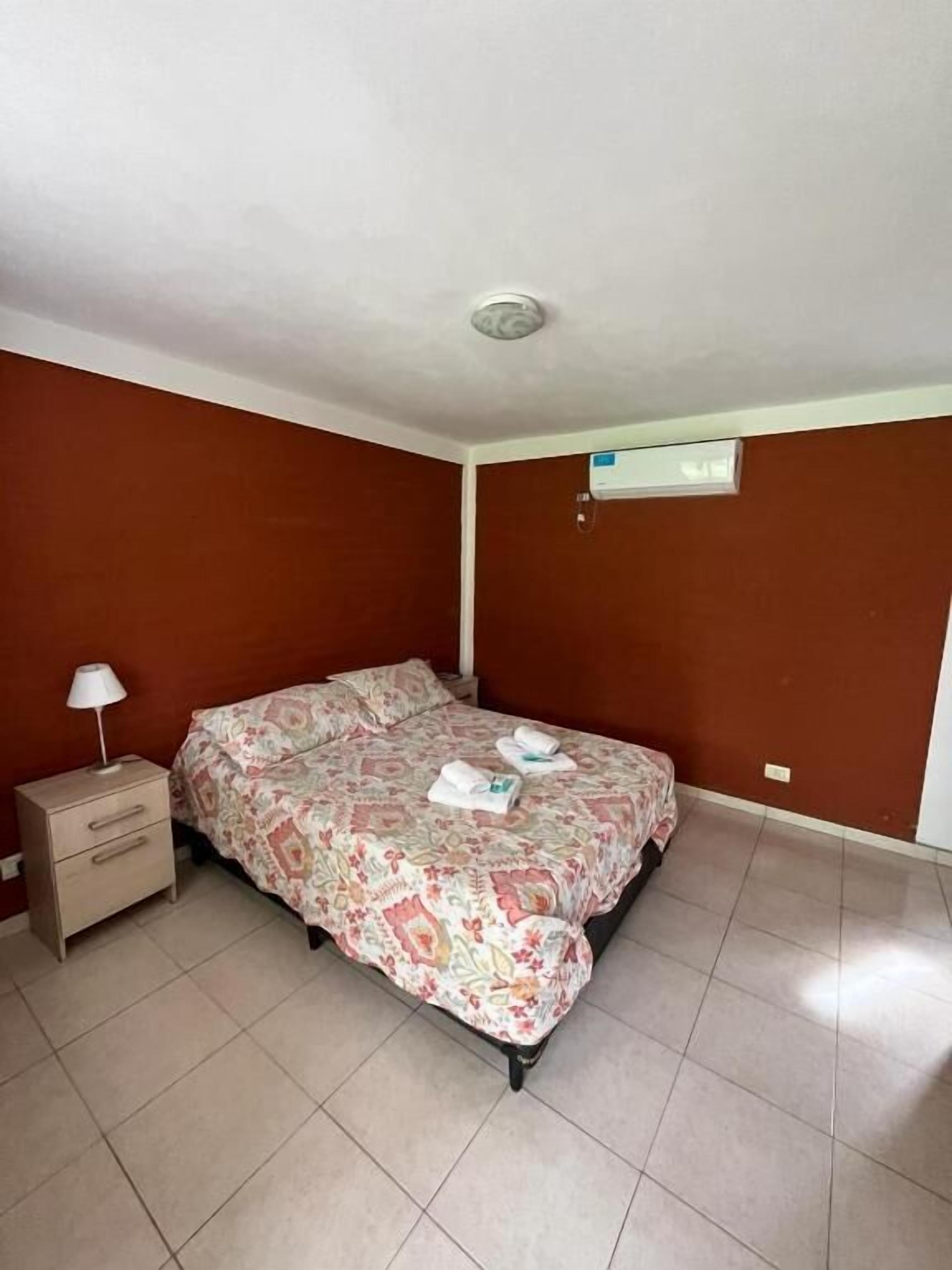 Un dormitorio con cama, mesita de noche y aire acondicionado instalado en la pared.