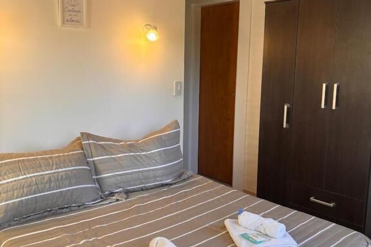 A hotel room with a bed, pillows, a wardrobe, and a wall-mounted light fixture.