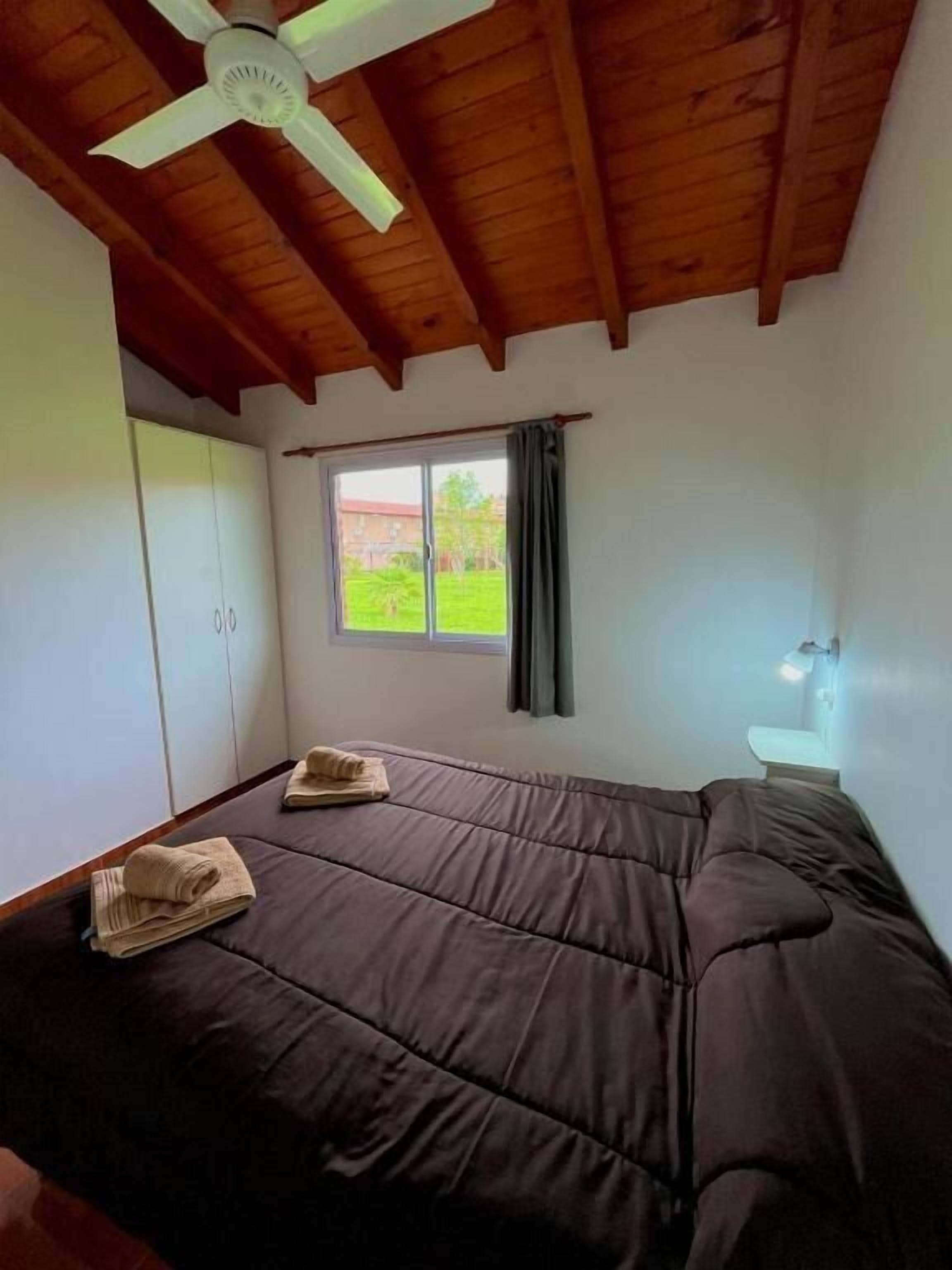 Une chambre avec un lit, un ventilateur de plafond, une fenêtre avec des rideaux et une lampe de chevet.