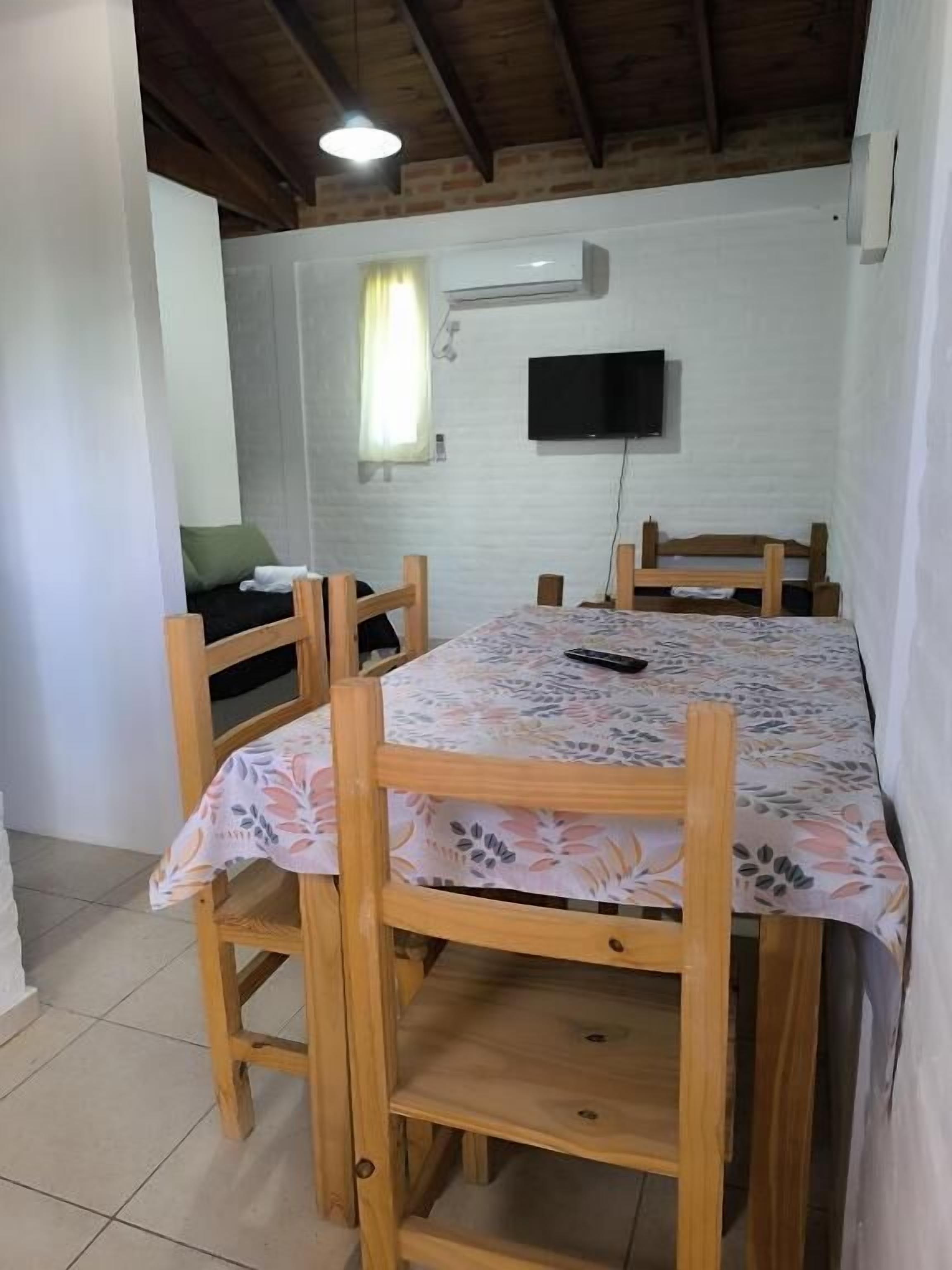 A dining area with a table and chairs, a television mounted on the wall, and a window with curtains.