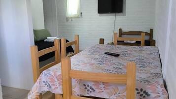 A dining area with a table and chairs, a television mounted on the wall, and a window with curtains.