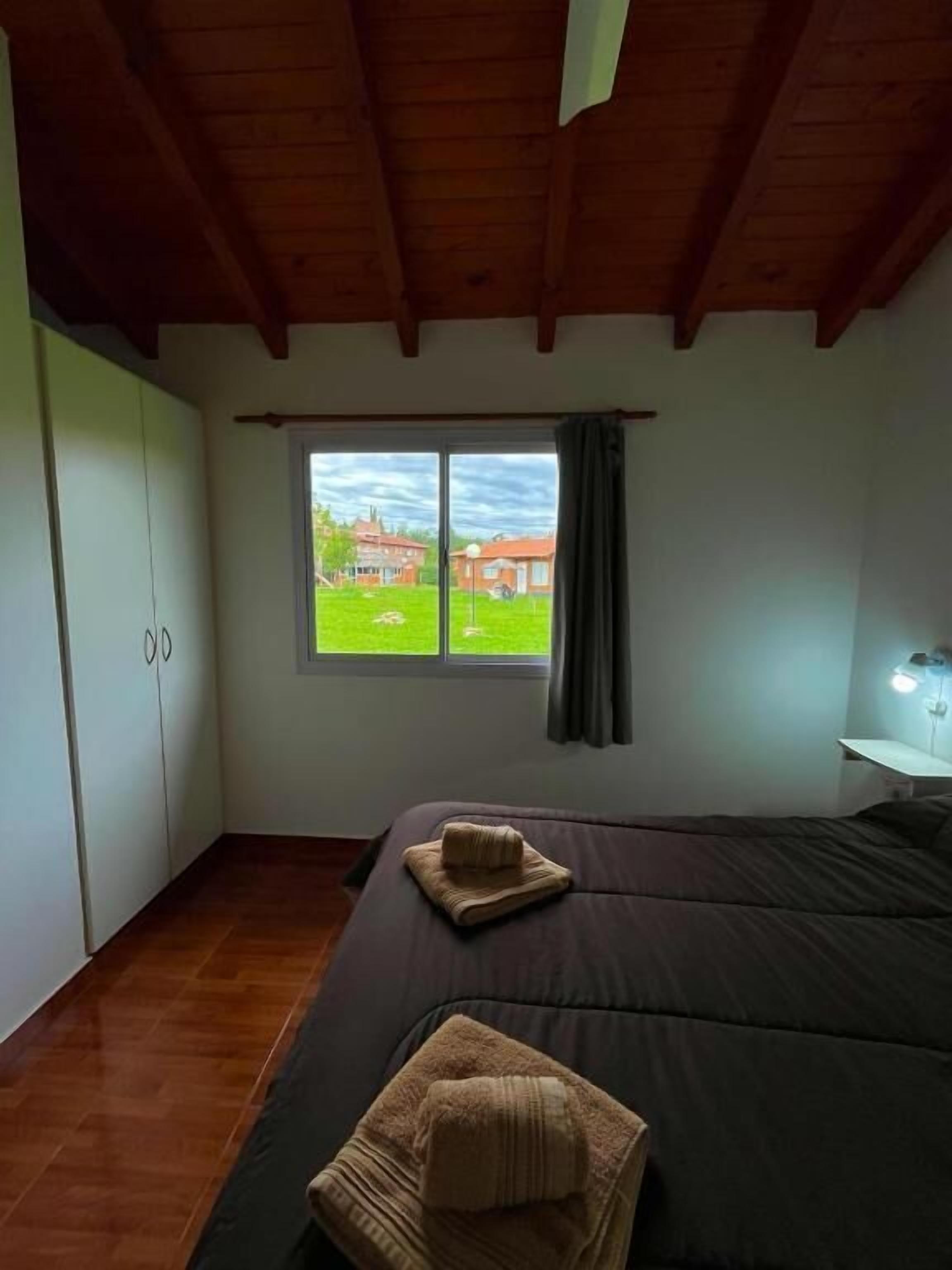 A bedroom with a large bed, a window with a view, a wardrobe, and a bedside table.