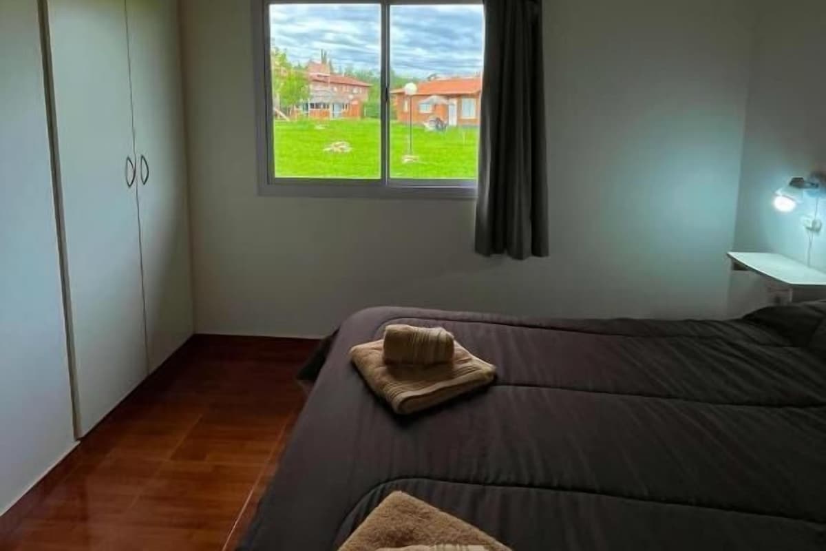 A bedroom with a large bed, a window with a view, a wardrobe, and a bedside table.