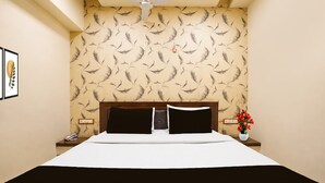 Una habitación de hotel con una cama, una mesita de noche y un ventilador de techo. En la pared, un diseño con motivos de plumas.