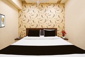 A hotel room with a bed, a nightstand, a bedside table, a ceiling fan, and a wall with a feather pattern.