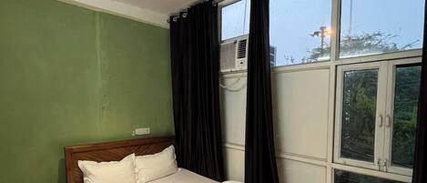 Un dormitorio con cama, mesita de noche, ventilador de techo y una ventana grande.