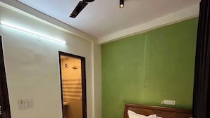 A hotel room with a bed, a ceiling fan, a green wall, and a bathroom visible through an open door. - Vida Stays (New Delhi)