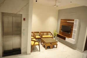 Una sala de estar moderna con una mesa de centro de madera, sillas a juego, un televisor de pantalla plana montado en un panel de madera y un ascensor al fondo.