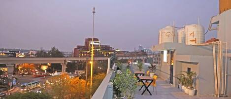 A rooftop terrace with potted plants, outdoor seating, and a view of the cityscape.