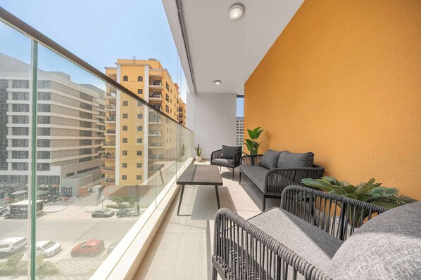 A balcony with a sofa, a small table, and potted plants. - StayShort - Bright & Roomy 2 bed with Balcony that Sleeps 6 (Majan)