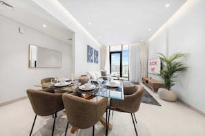 A modern dining area with a glass table, brown chairs, and a view of the city through large windows. - StayShort - Bright & Roomy 2 bed with Balcony that Sleeps 6 (Majan)
