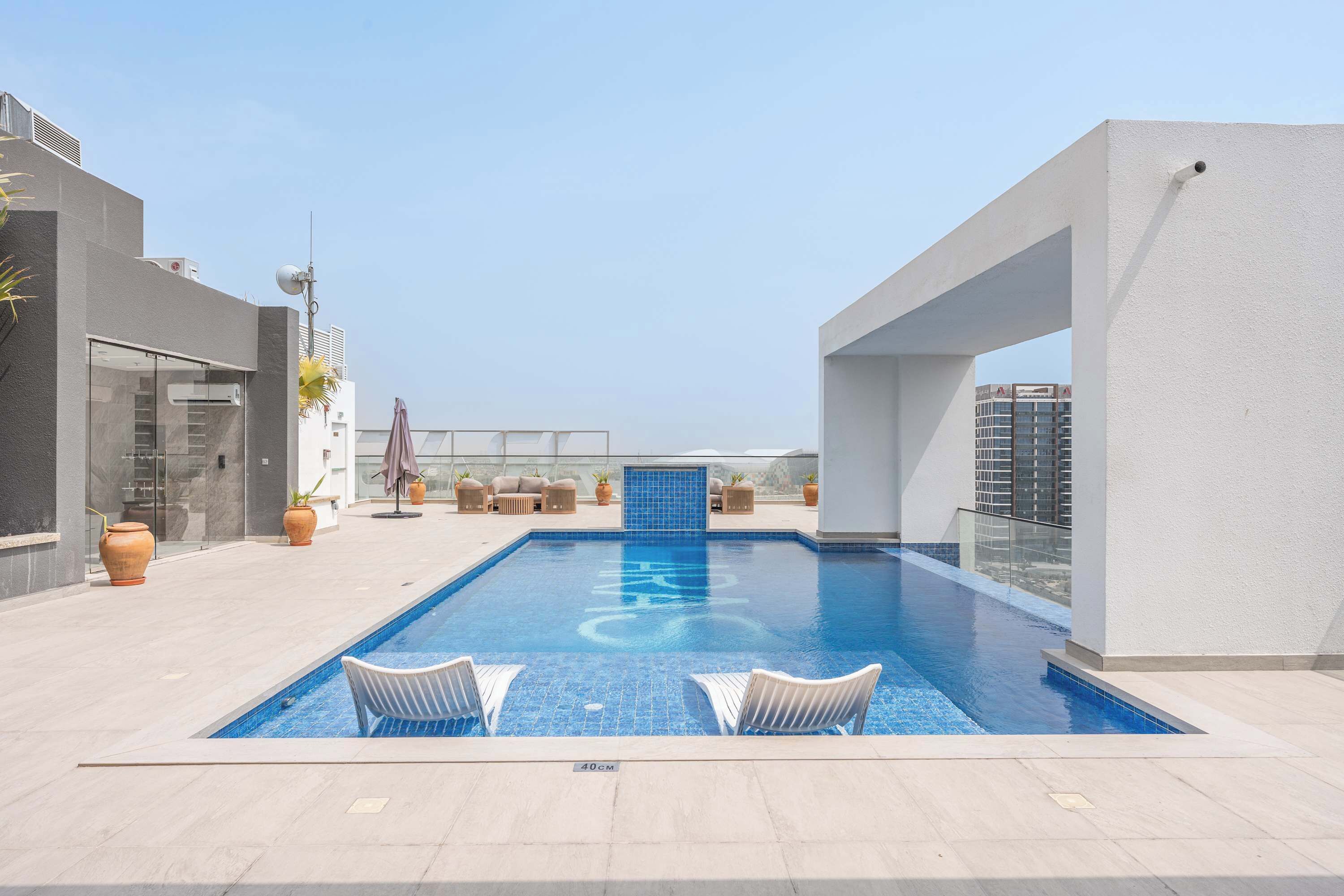 A rooftop swimming pool with a clear blue water feature, surrounded by modern outdoor furniture and potted plants.
