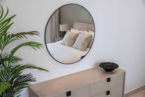 A bedroom with a bed, a bedside table, a lamp, a mirror, and a potted plant. - StayShort - Bright & Roomy 2 bed with Balcony that Sleeps 6 (Majan)