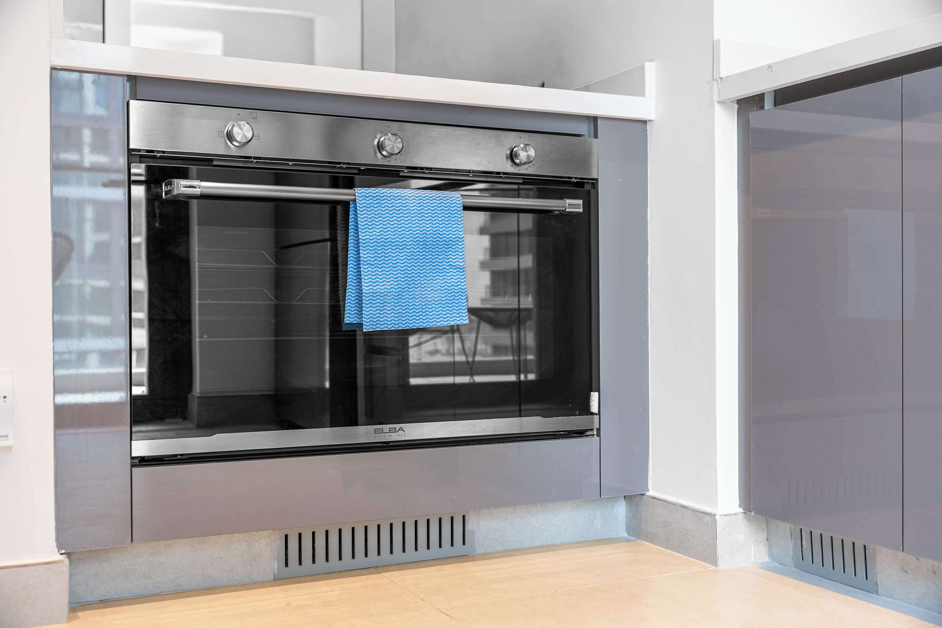 A modern kitchen with a built-in oven, a stainless steel range hood, and a blue towel hanging on the oven door.