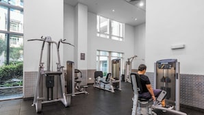 Ein Fitnessstudio mit verschiedenen Trainingsgeräten, großen Fenstern und Blick auf Grünflächen.