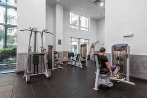 Ein Fitnessstudio mit verschiedenen Trainingsgeräten, großen Fenstern und Blick auf Grünflächen.
