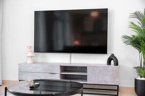 A modern living room with a flat-screen TV mounted on a wall, a minimalist console table, and a potted plant. - StayShort - Comfortable Studio in Downtown with Burj Khalifa Views! (Downtown)