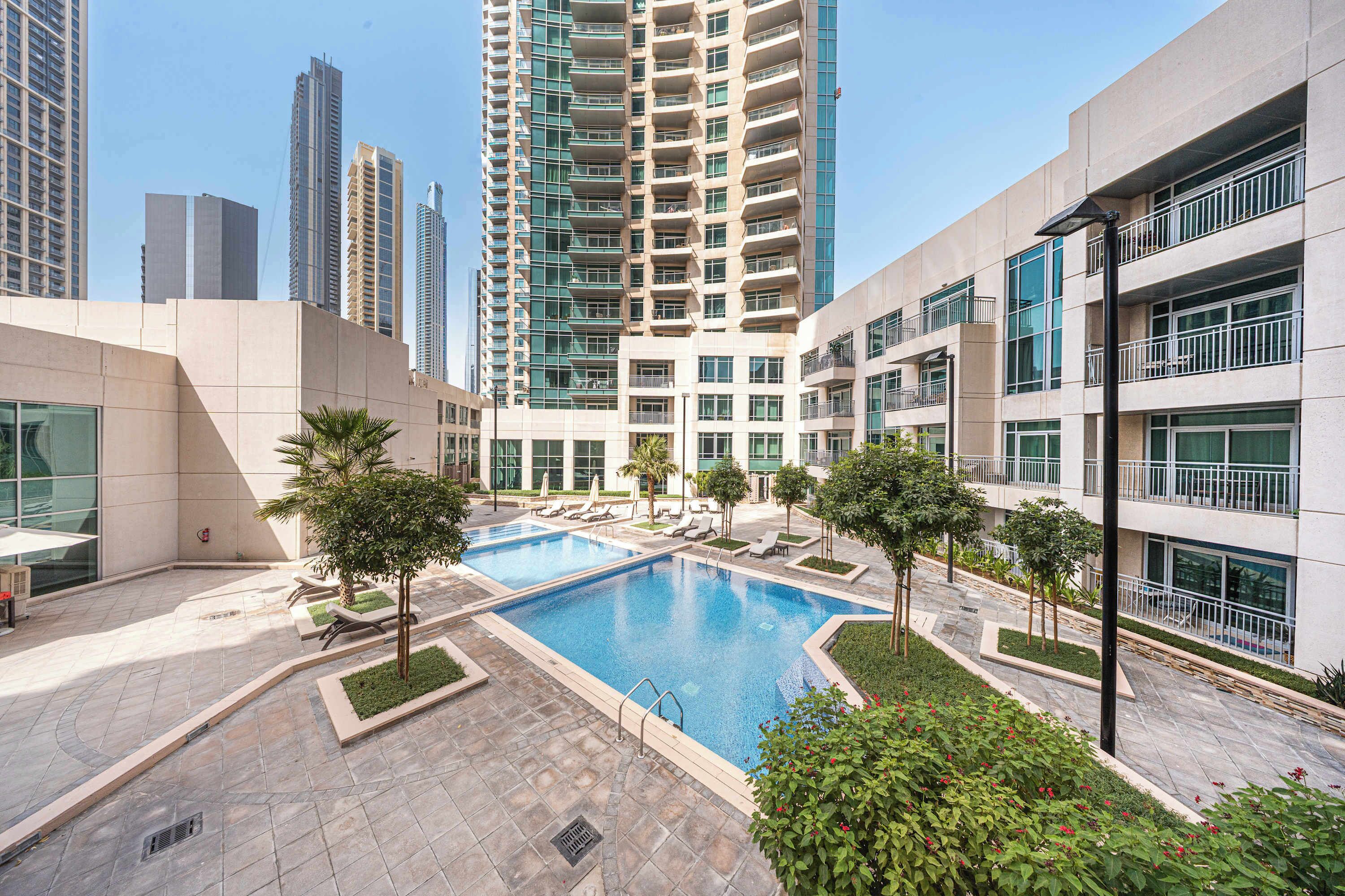 Un edificio residencial moderno con piscina, sillones de descanso y un jardín bien cuidado.