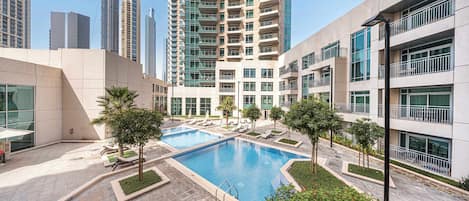 A modern residential building with a swimming pool, lounge chairs, and a well-maintained garden.