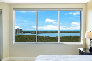 Ein Schlafzimmer mit großem Fenster und Blick auf einen See sowie Gebäude.