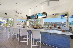 Eine Bar mit mehreren Bildschirmen, Barhocker und Blick auf den Strand.