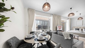 Ein modernes Wohnzimmer mit Essbereich, grauen Sofas, einem Esstisch gedeckt mit Tellern und Gläsern, und einem Schild mit der Aufschrift 'BOOK ME'.