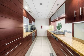 A modern kitchen with wooden cabinets, granite countertops, stainless steel appliances, and a tiled floor. - StayShort - Luxury Studio Apartment in Downtown with Balcony (Downtown)
