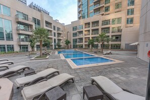 A courtyard with a swimming pool, lounge chairs, and a building with multiple balconies. - StayShort - Luxury Studio Apartment in Downtown with Balcony (Downtown)