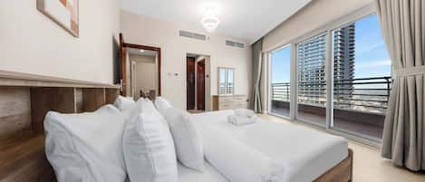 A hotel room with a large bed, a wooden headboard, a view of the city through the window, and a balcony with a railing.