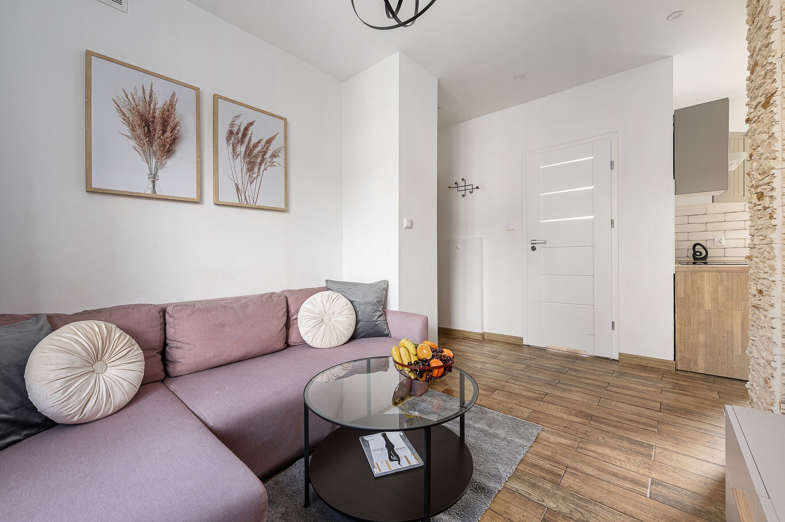 A modern living room with a sofa, a glass coffee table, and two framed botanical prints on the wall.
