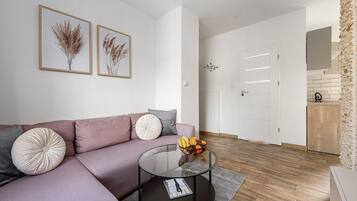 A modern living room with a sofa, a glass coffee table, and two framed botanical prints on the wall.