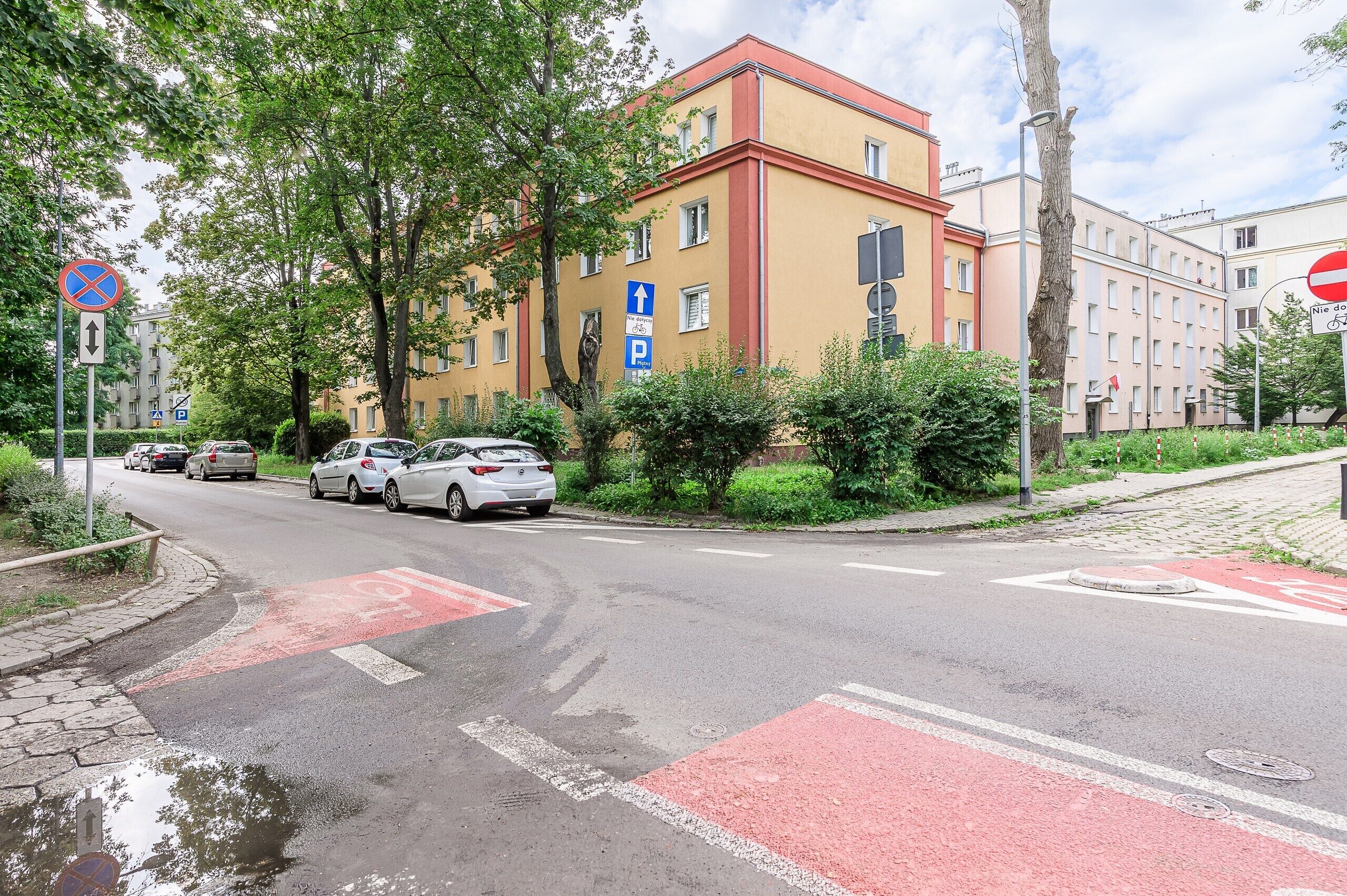 A street with parked cars, a pedestrian crossing, and a building with multiple windows.